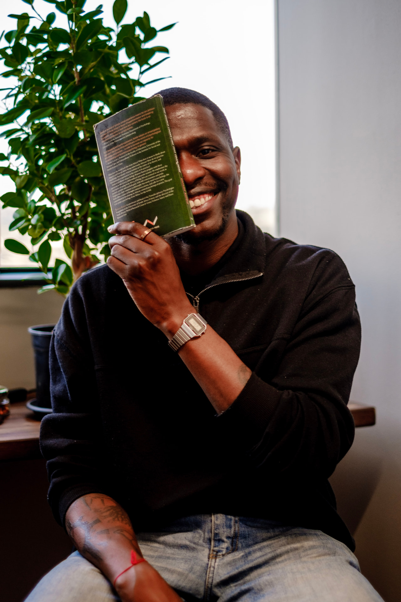 Obert Rukato, clinical psychologist, smiling warmly while holding a book in his Johannesburg consulting room